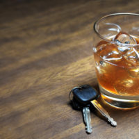 Glass of whiskey and car keys on wooden table.