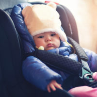 Adorable little girl sitting in car with winter clothes and jacket