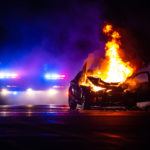 Car on fire at night with police lights in background Car on fire at night with police lights in background