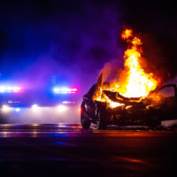 Car on fire at night with police lights in background Car on fire at night with police lights in background