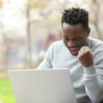 Excited black man checking laptop in a park Excited black man checking laptop in a park