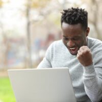 Excited black man checking laptop in a park Excited black man checking laptop in a park