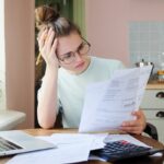Indoor shot of young European Caucasian girl looking at financial documents at home with deeply bored face looking sick and tired of her economic problems, trying to check counts and all details Indoor shot of young European Caucasian girl looking at financial documents at home with deeply bored face looking sick and tired of her economic problems, trying to check counts and all details