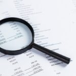 Magnifying glass on financial statement paper. Analyzing business financial data. Magnifying glass on financial statement paper. Analyzing business financial data.
