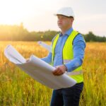 Architect looking at blueprints and inspecting new building land plot
