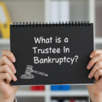 Close Up Hands Holding Black Notebook with Text What is a Trustee In Bankruptcy in a Bright Office