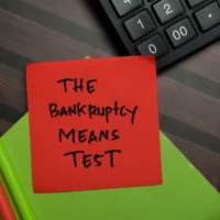 The Bankruptcy Means Test write on sticky notes isolated on Wooden Table.